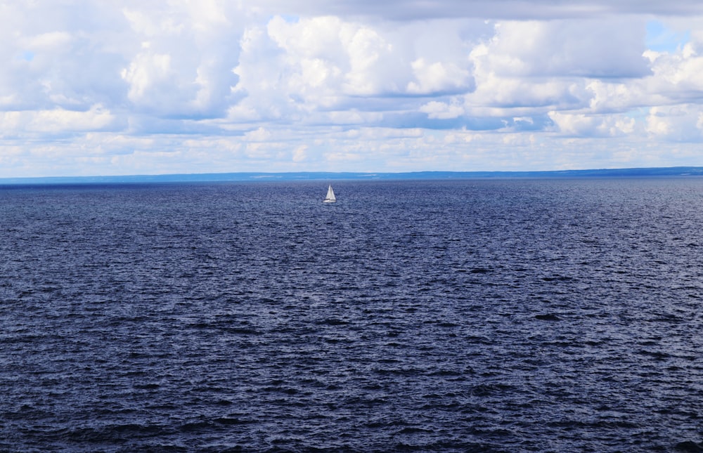 weißes Segelboot auf See unter weißen Wolken und blauem Himmel tagsüber