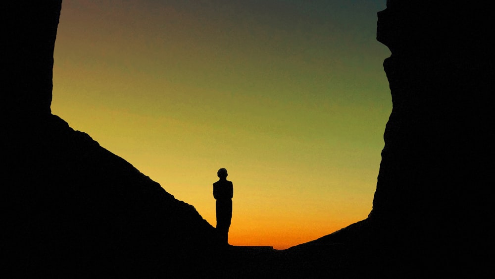Silueta del hombre de pie sobre la formación rocosa durante la puesta del sol