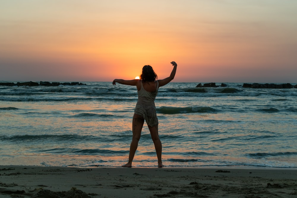 woman in white tank top and gray shorts standing on seashore during sunset