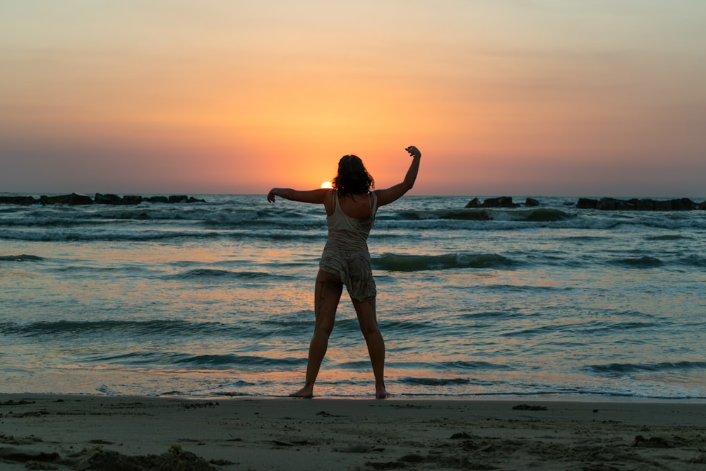 Frau in weißem Tanktop und grauen Shorts bei Sonnenuntergang am Meeresufer