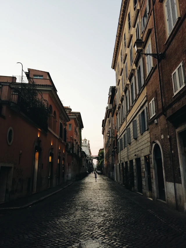 Via Giulia's straight cobblestone street at dusk with a distant dome visible at the vanishing point