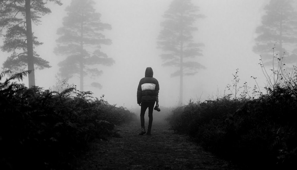 grayscale photo of man in backpack walking on pathway