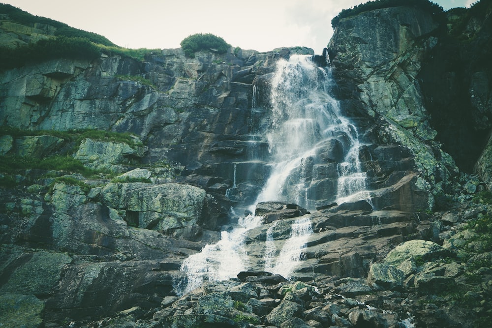 waterfalls on rocky mountain under white sky during daytime