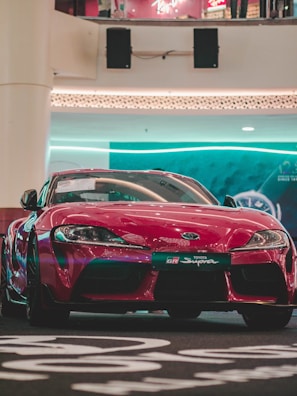 Sleek red sports car parked under bright showroom lights.
