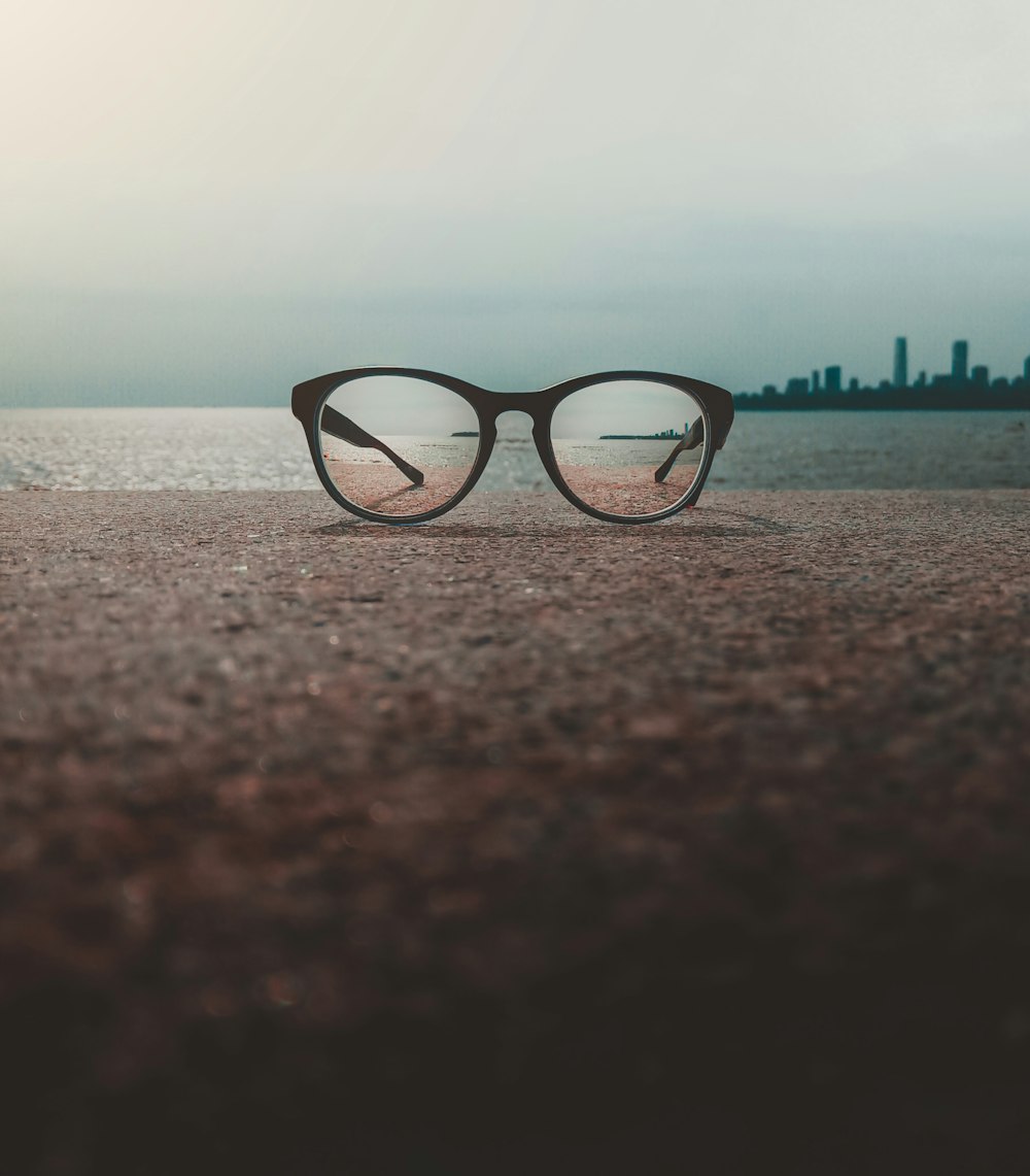 black framed eyeglasses on brown sand near body of water during daytime