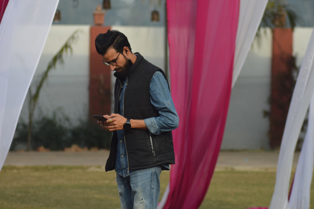 man in black jacket and blue denim jeans standing near red textile