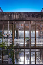 A sleek modern building with large glass windows reflecting the sky, surrounded by lush greenery.