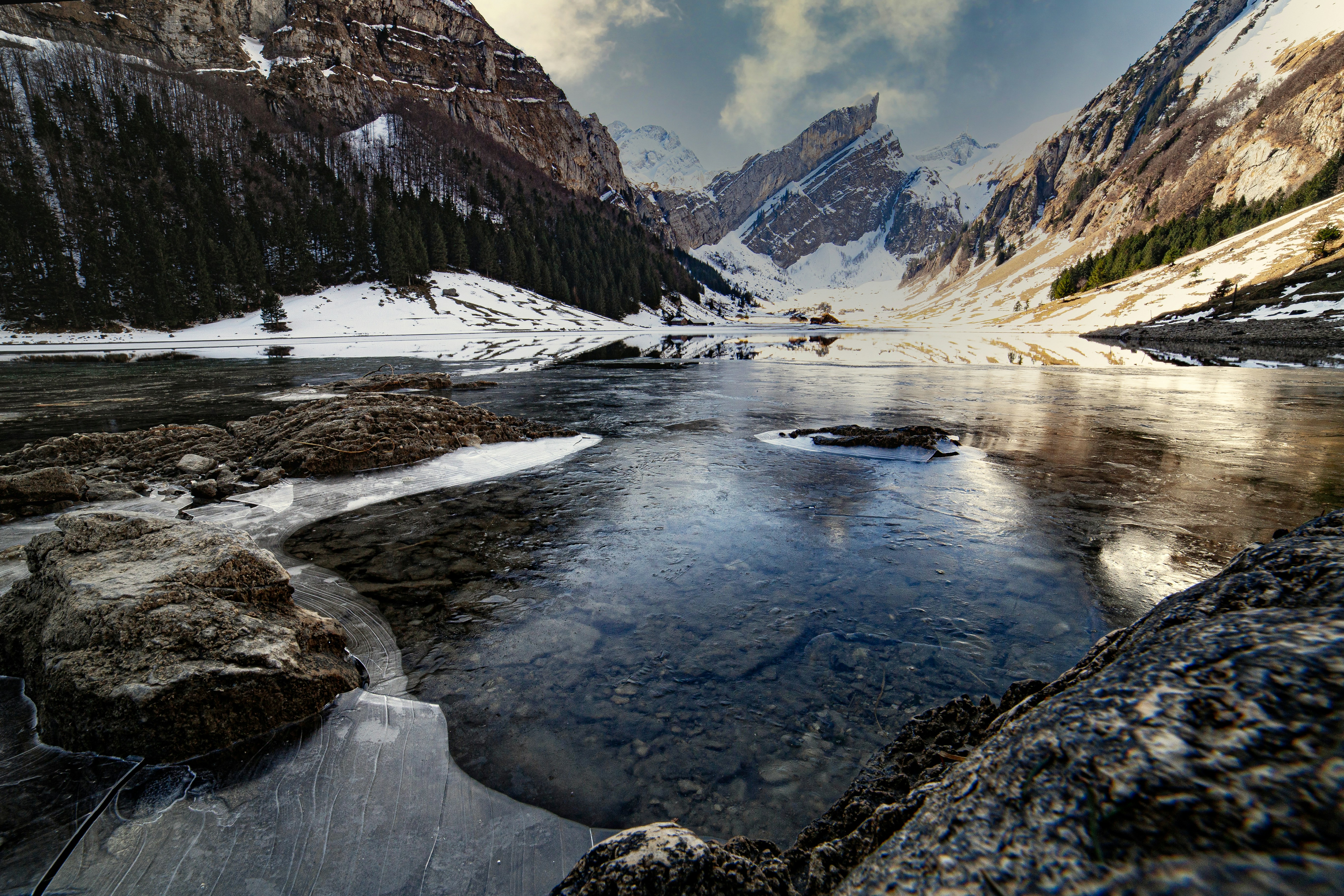 Kashmir snow mountains with frozen lake and dark pine forest in overcast light