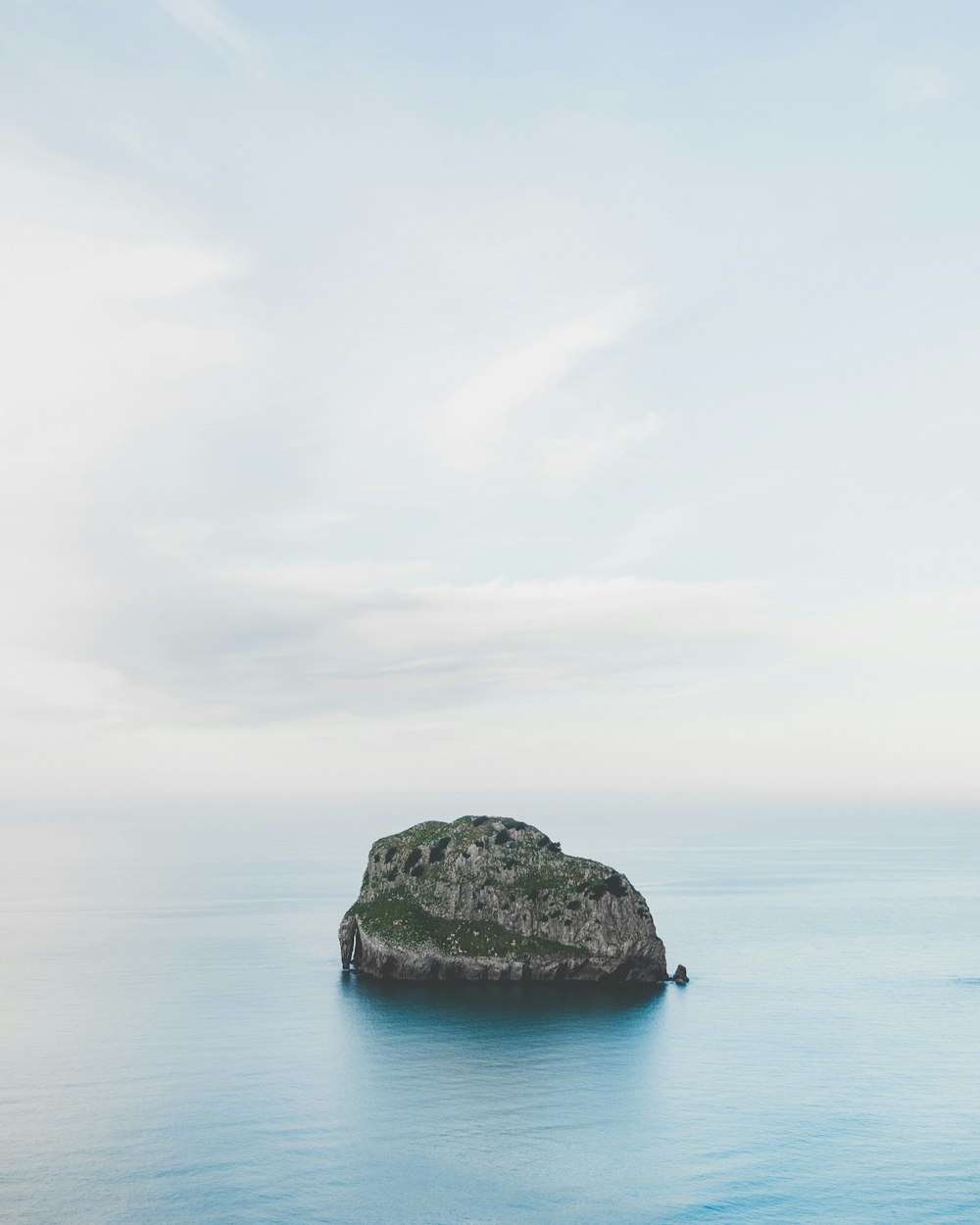 gray rock formation on blue sea under white clouds during daytime