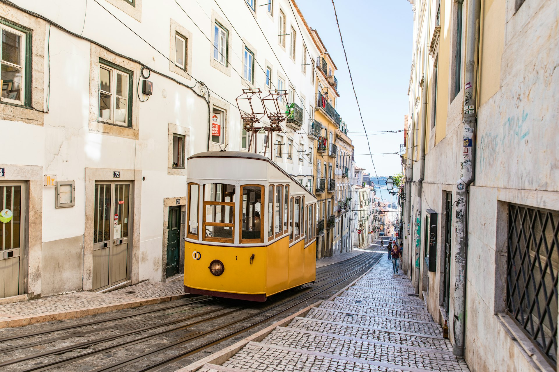 Yellow funicular tram climbing a narrow cobblestone street in Lisbon, Portugal