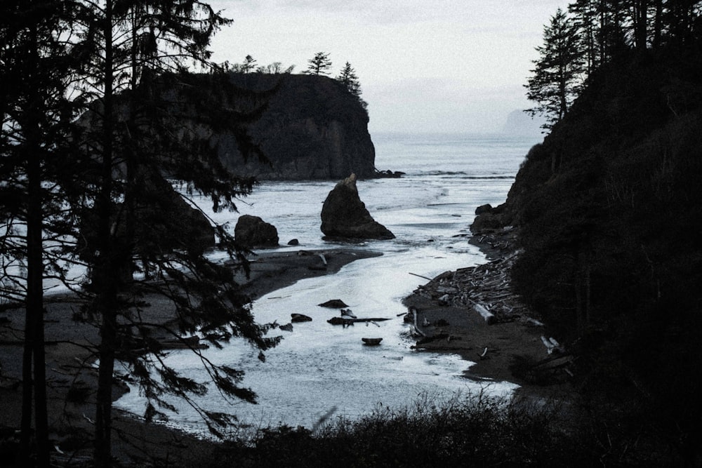 grayscale photo of rocky mountain near body of water