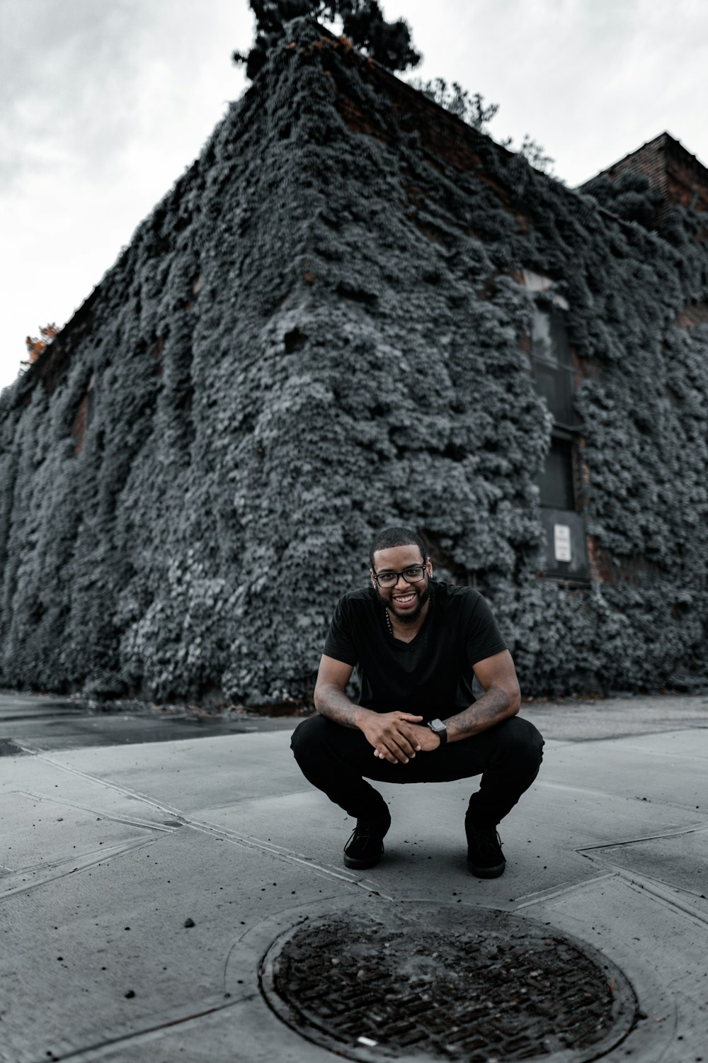 Mann in schwarzem Rundhals-T-Shirt und schwarzer Hose sitzt auf grauem Betonboden