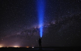 silhouette of man standing on seashore under starry night