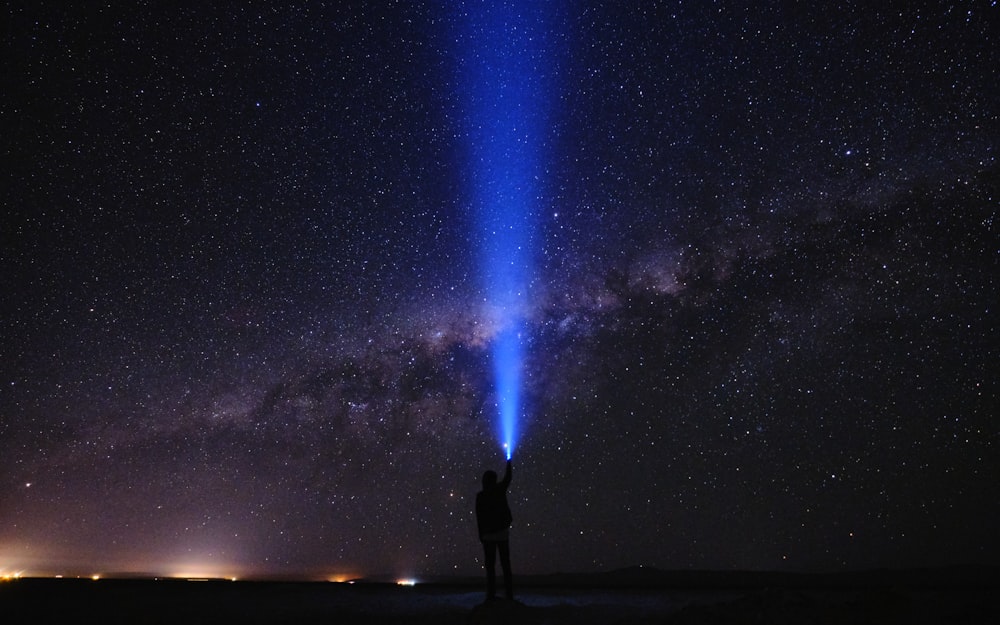 Silhouette eines Mannes, der unter sternenklarer Nacht am Meeresufer steht