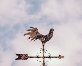 A handcrafted copper rooster weathervane shining under the sun atop a rustic barn roof.