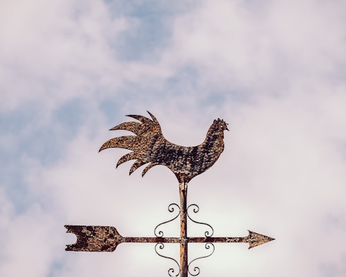 A handcrafted copper rooster weathervane shining under the sun atop a rustic barn roof.