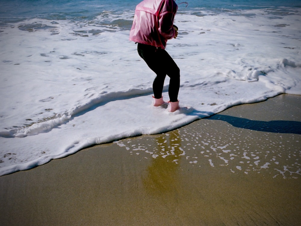 woman in pink hoodie and black pants standing on beach shore during daytime