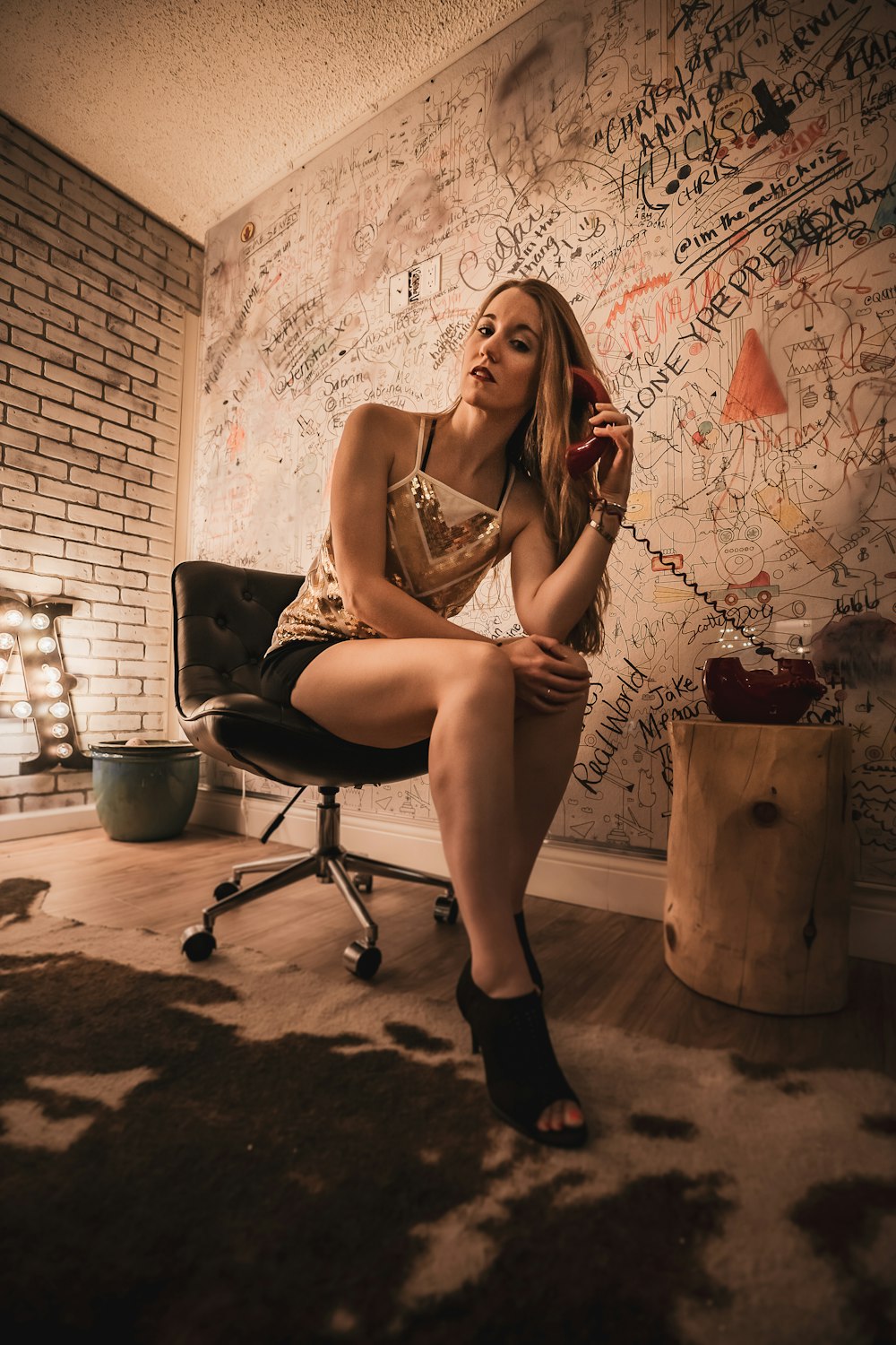 Femme en robe à bretelles spaghetti blanche et noire assise sur une chaise roulante de bureau noire