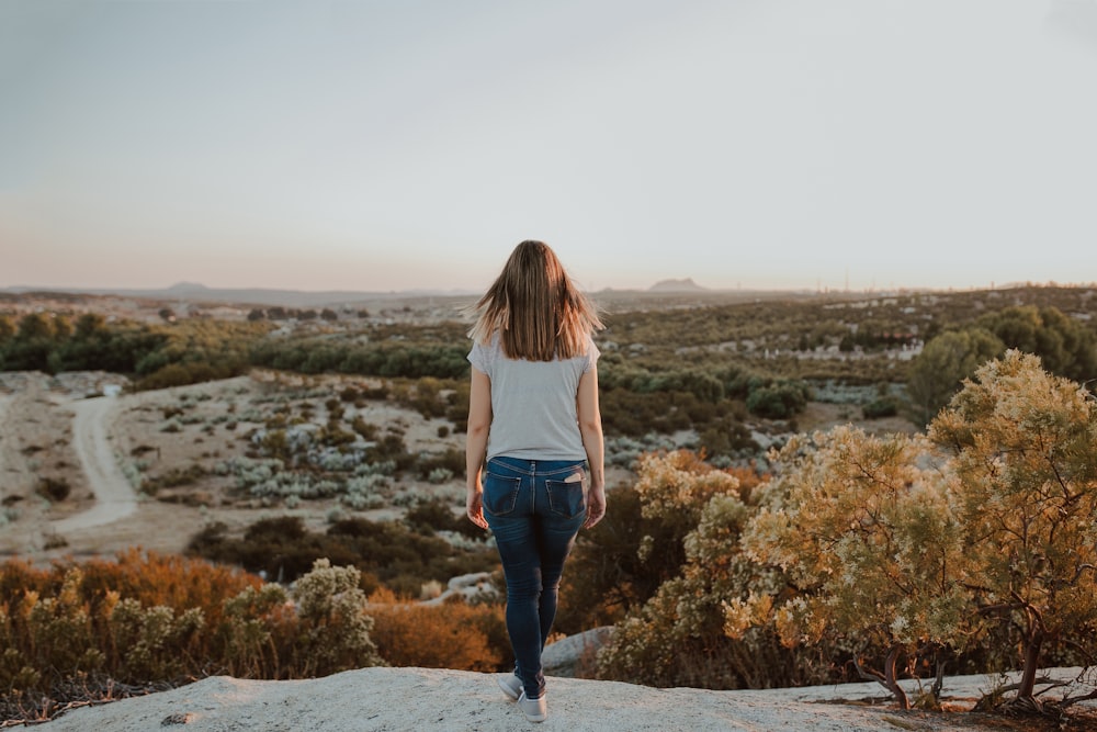 woman in white long sleeve shirt and blue denim jeans standing on gray rock during daytime