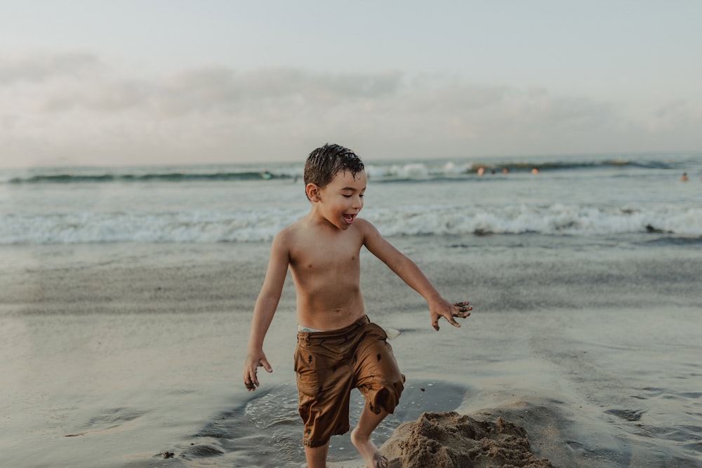menino em shorts marrons em pé na praia durante o dia