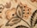 Intricate floral embroidery with detailed patterns in shades of orange, beige, and black. Large leaves and blooming flowers create a vintage and artistic appearance.