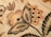 Intricate floral embroidery with detailed patterns in shades of orange, beige, and black. Large leaves and blooming flowers create a vintage and artistic appearance.