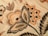 Intricate floral embroidery with detailed patterns in shades of orange, beige, and black. Large leaves and blooming flowers create a vintage and artistic appearance.