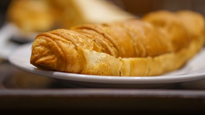 Close-up of a freshly baked golden croissant with flaky layers on a bright ceramic plate.