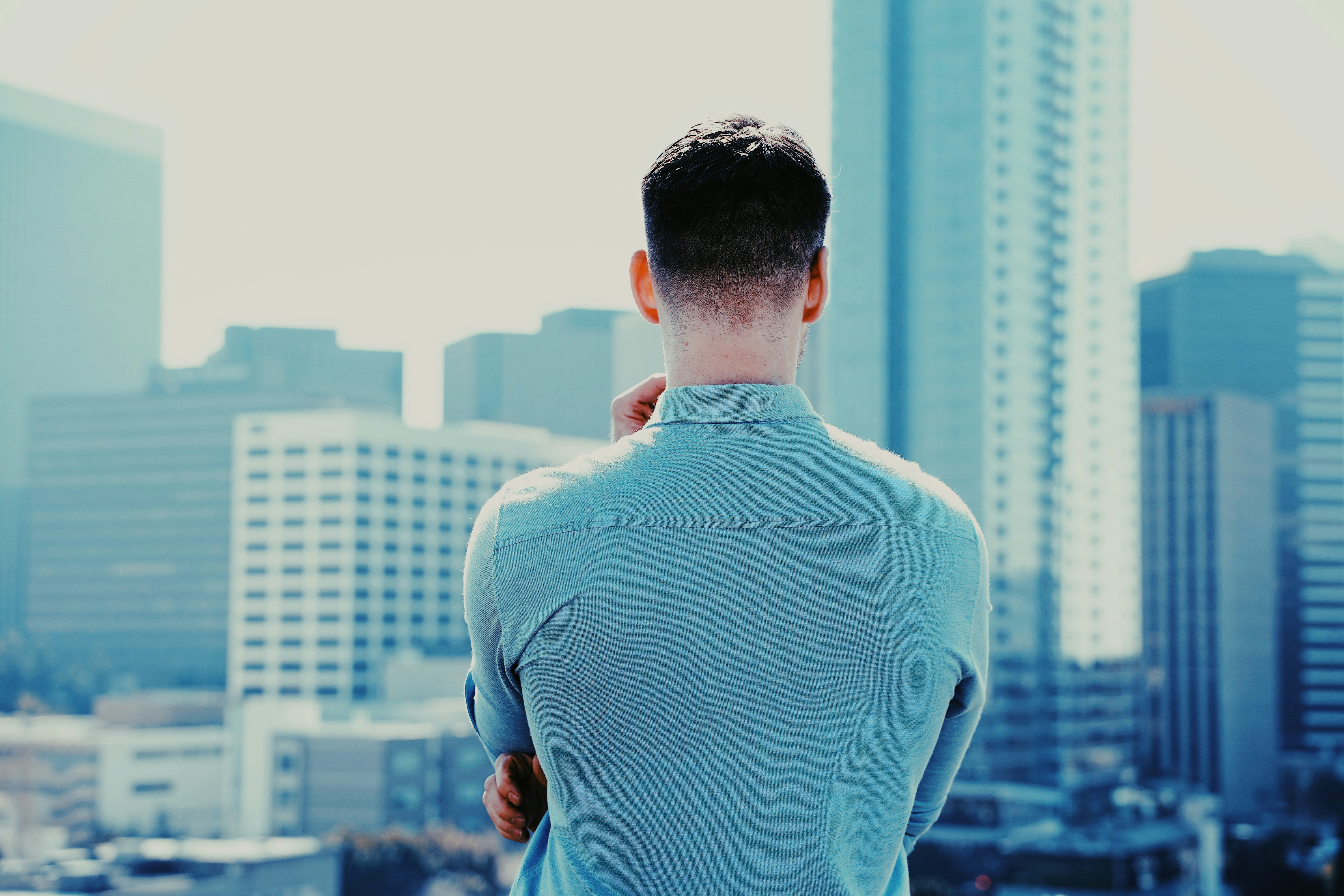 man in blue long sleeve shirt standing in front of city buildings during daytime