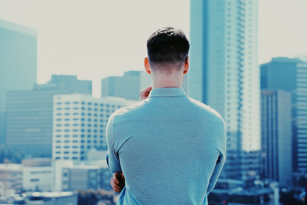 man in blue long sleeve shirt standing in front of city buildings during daytime