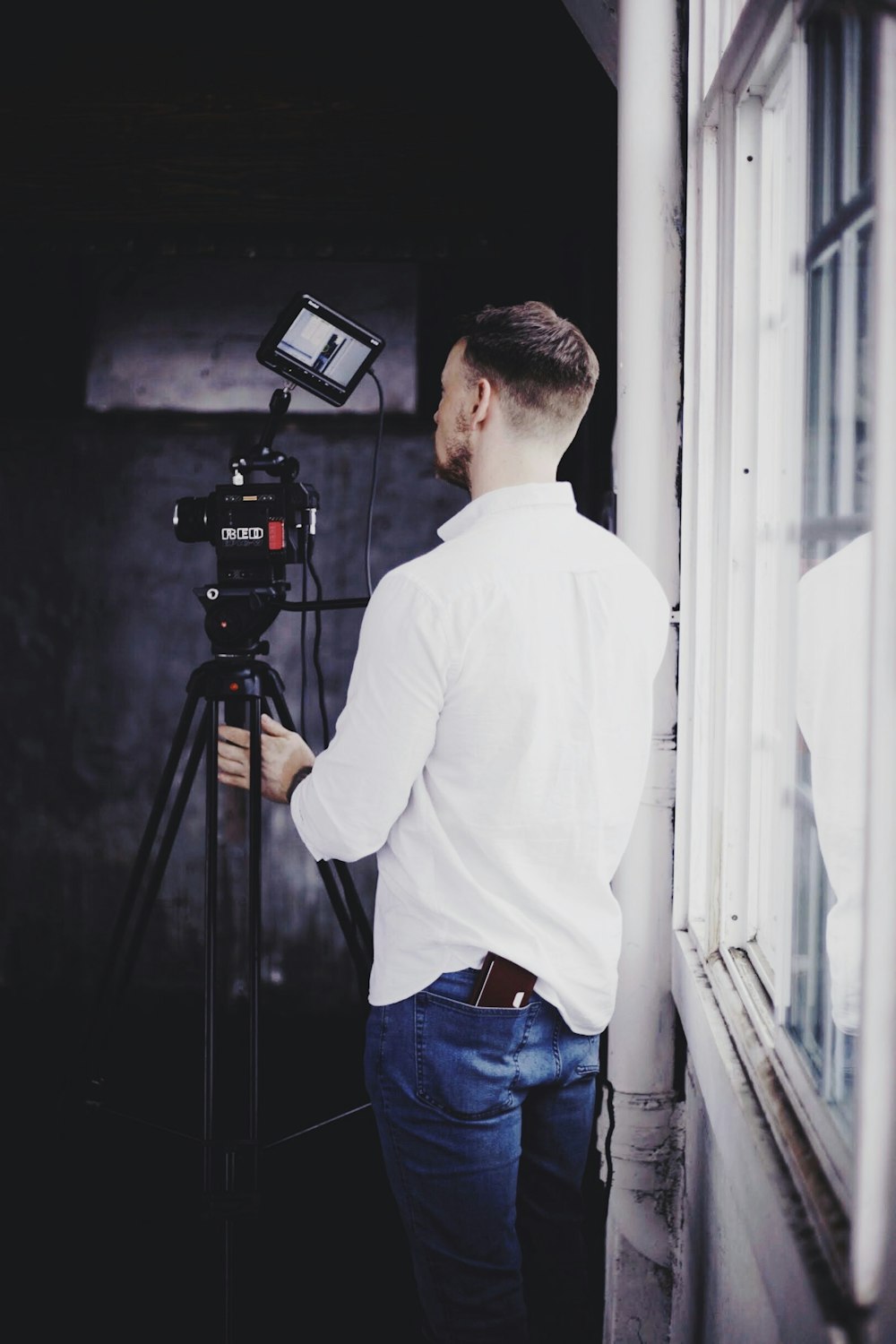 man in white long sleeve shirt and blue denim jeans standing in front of black camera