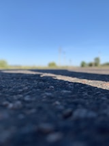 Close-up of freshly laid asphalt with visible road lines under a clear blue sky.