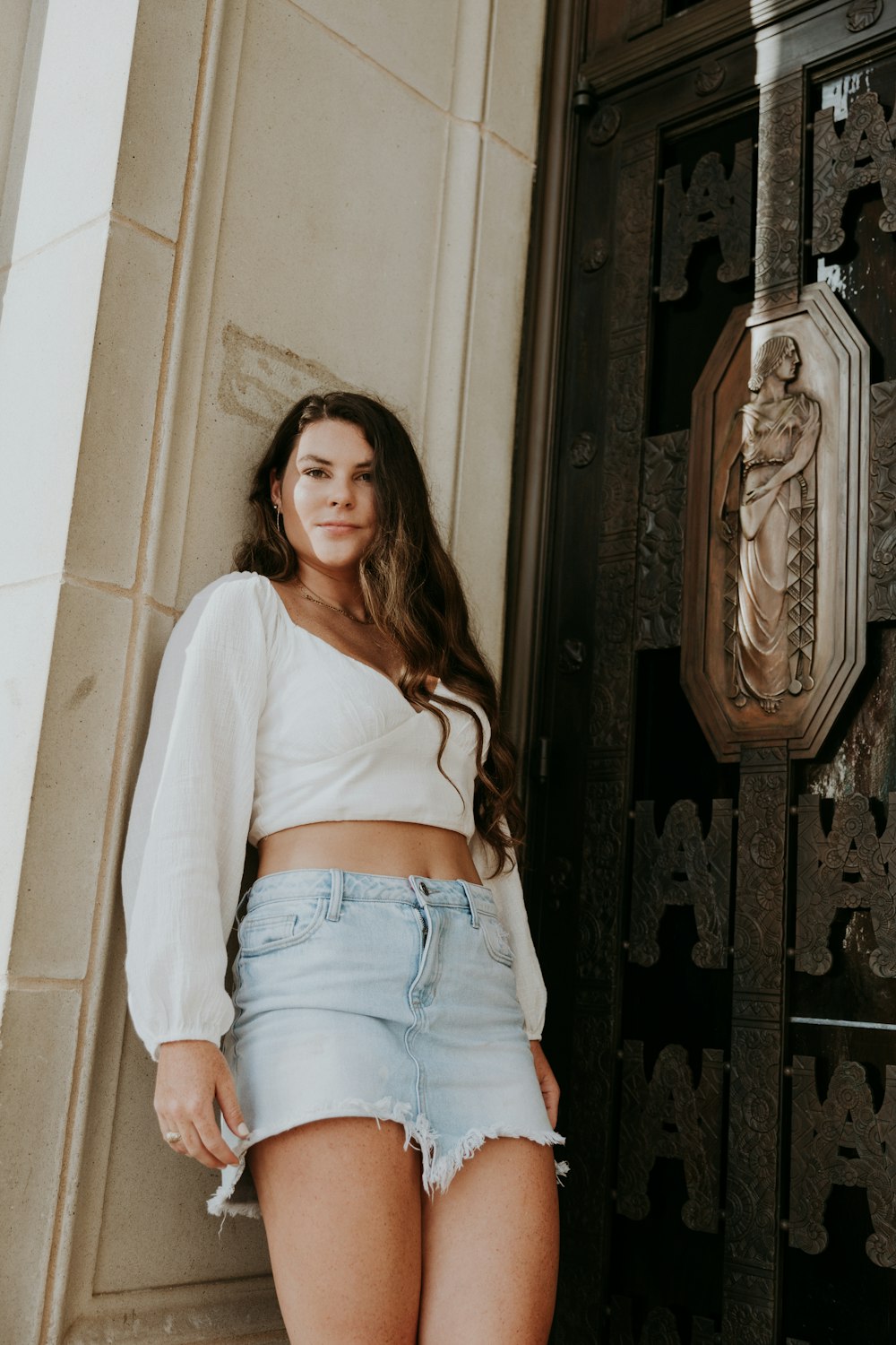 woman in white long sleeve shirt and blue denim shorts standing beside brown wooden door