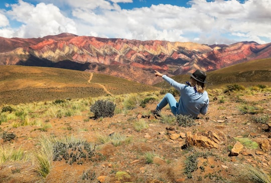 man in white long sleeve shirt and black pants sitting on brown rock during daytime in Jujuy Argentina