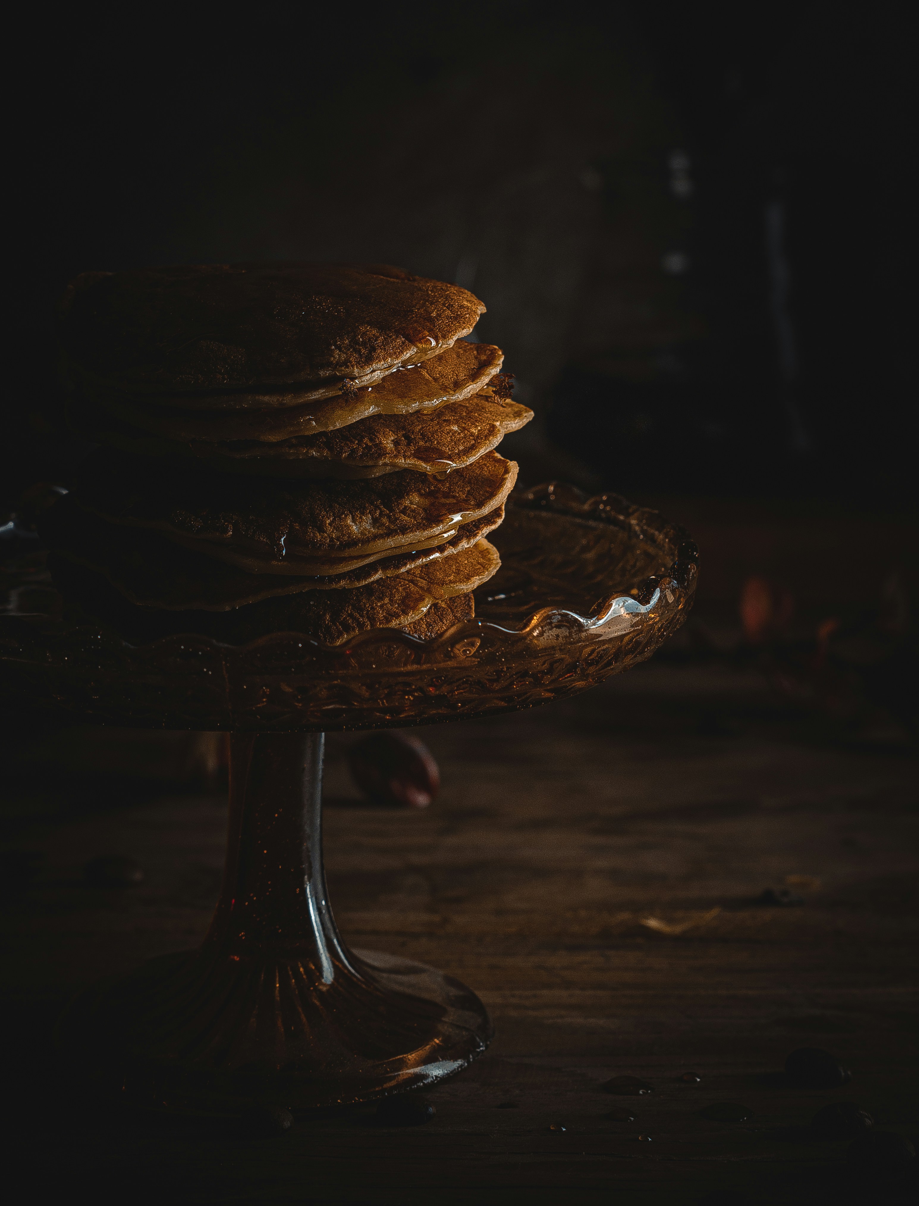 Stacked pancakes with dark syrup drizzle, moody dark background