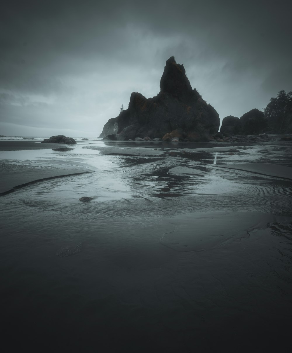 rock formation on body of water under cloudy sky