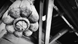 A large, intricately carved wooden ornament resembling a flower is attached to a wooden structure. The texture of the wood is rough and weathered, highlighting cracks and grain patterns. The background consists of wooden beams and planks, adding an architectural element.