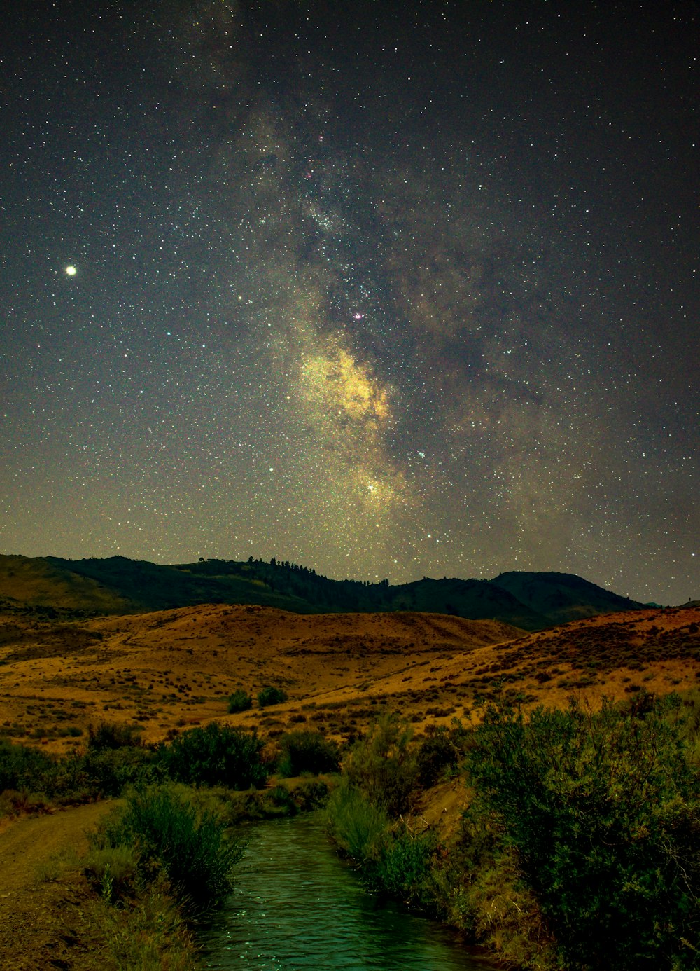 a river running through a lush green field under a night sky