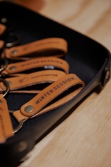 A set of leather keychains on a tray with the text 'Winter Session' and 'Made in Denver' embossed on them.