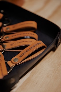 A set of leather keychains on a tray with the text 'Winter Session' and 'Made in Denver' embossed on them.