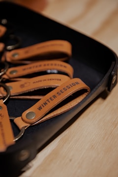 A set of leather keychains on a tray with the text 'Winter Session' and 'Made in Denver' embossed on them.