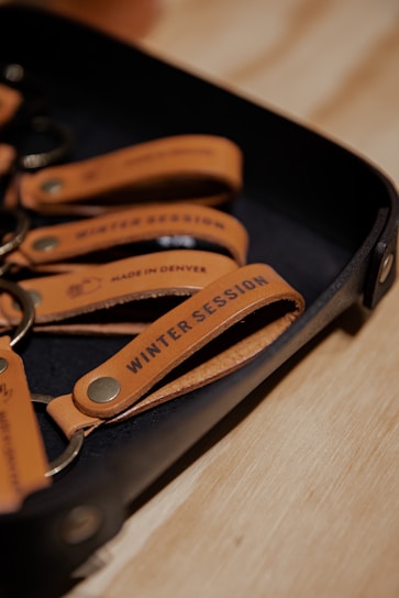 A set of leather keychains on a tray with the text 'Winter Session' and 'Made in Denver' embossed on them.