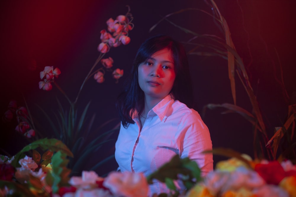 woman in pink dress shirt standing near red flowers