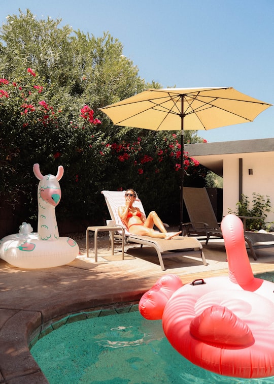 woman in white and red dress sitting on white and brown armchair under red umbrella during in Palm Springs United States