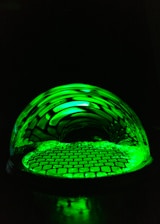 A glowing translucent green glass disc with a stylized 'ep' monogram surrounded by organic leaf shapes and soft golden light beams.