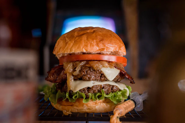 A stacked burger dripping with melted cheese, fresh lettuce, and tomato