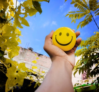 a hand holding a yellow smiley face ball