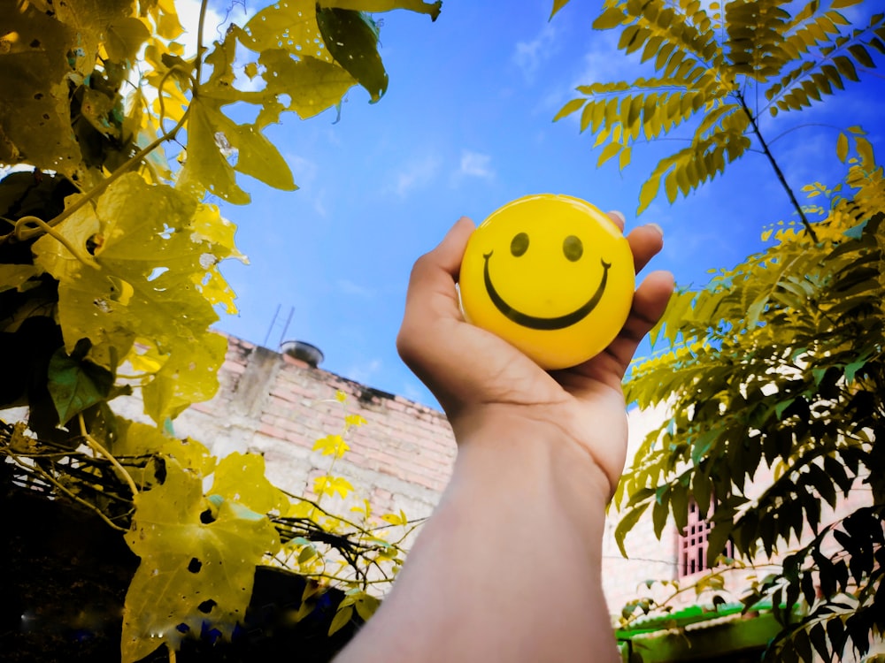 une main tenant une boule jaune souriante