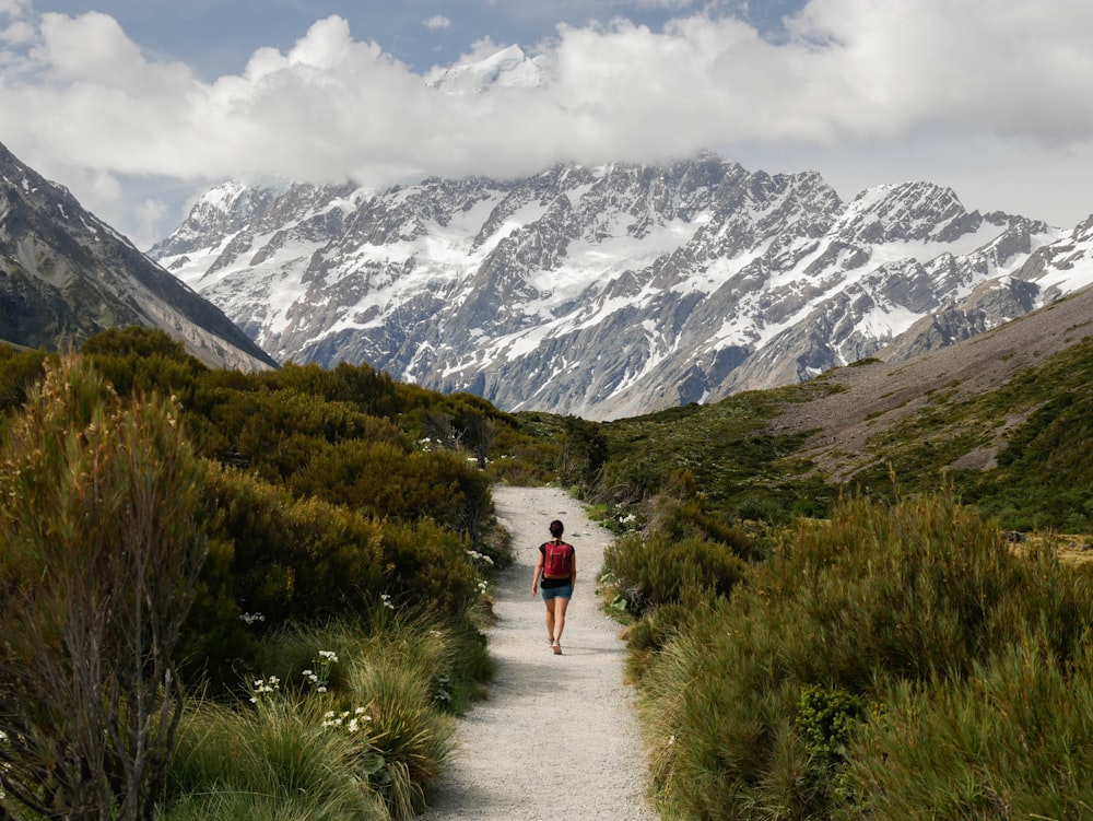 person in red jacket and gray pants walking on pathway near snow covered mountains during daytime