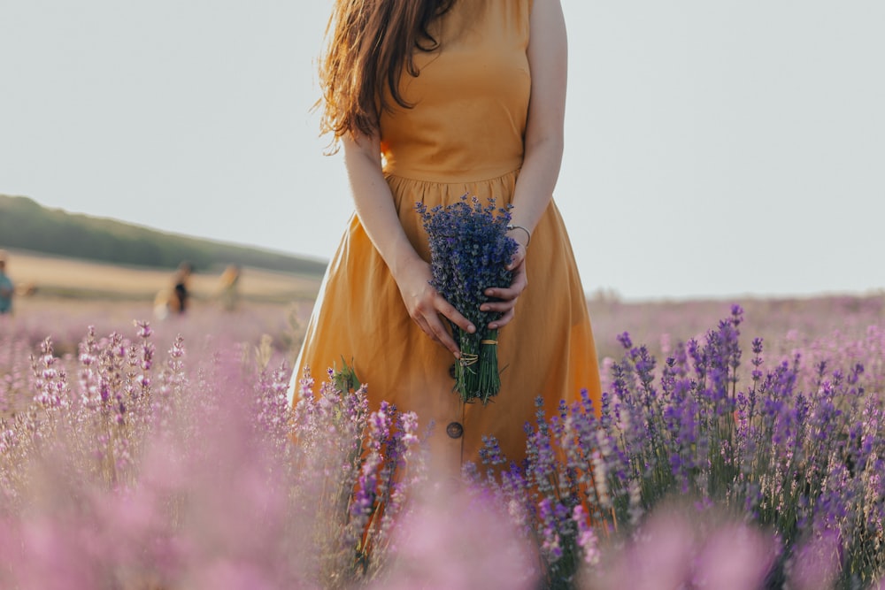femme en robe jaune sans manches tenant une fleur violette